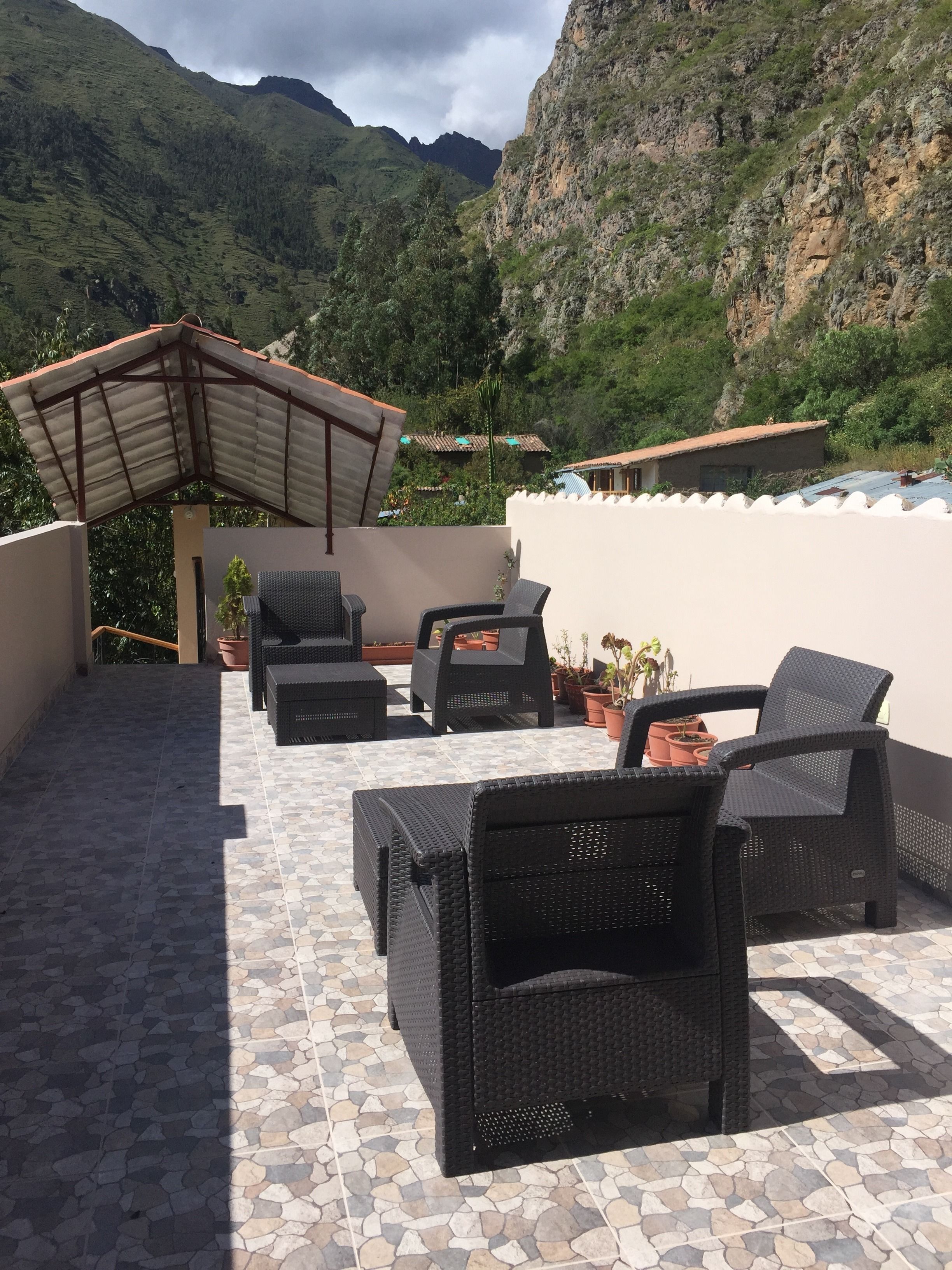 Un patio con mobiliario de mimbre, plantas en macetas y vistas a montañas.