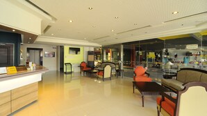 Eine Hotelhalle mit Empfangstresen, Sitzgelegenheiten und einer Glastrennwand.
