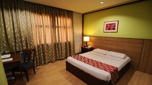 Ein Hotelzimmer mit einem großen Bett, einem Schreibtisch mit Stuhl, einem Nachttisch mit Lampe und einem Bild an der Wand.