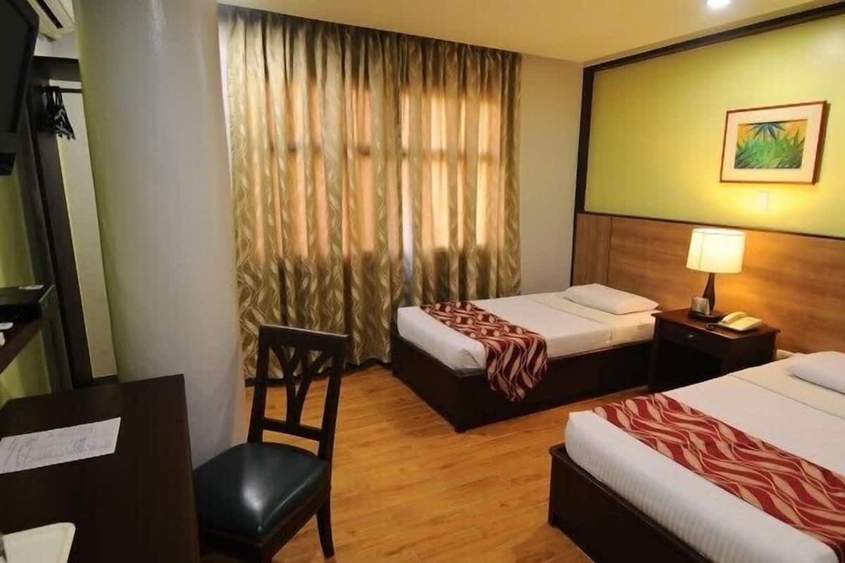 A hotel room with two beds, a desk, a chair, a lamp, and a painting on the wall.