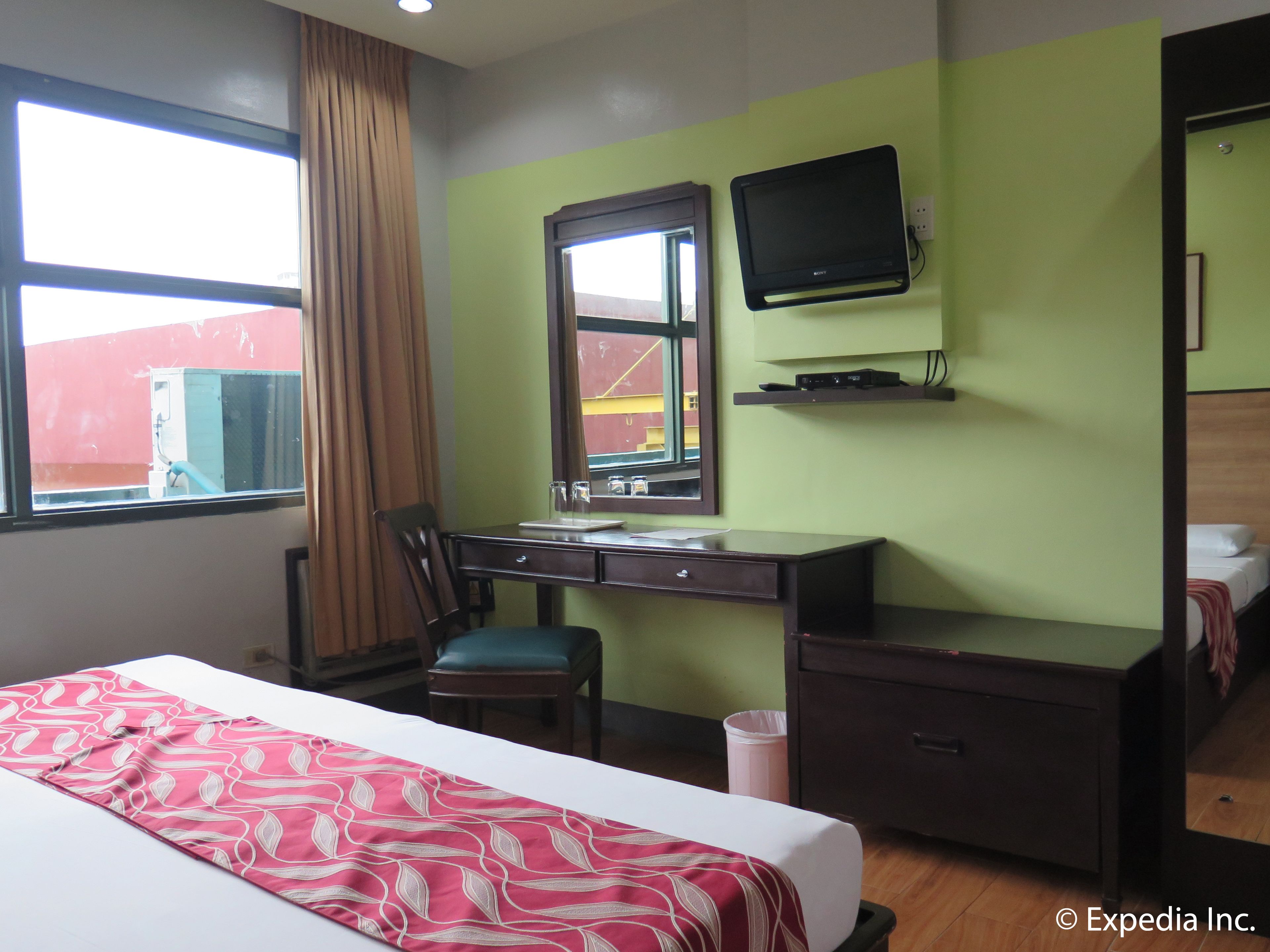 A hotel room with a bed, desk, chair, and a television on the wall.