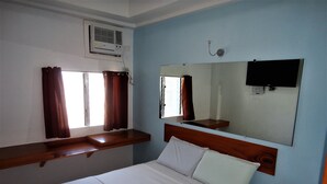Ein Hotelzimmer mit einem Bett, einem Wand-Fernseher, einem Fenster mit Vorhängen und einer Klimaanlage.