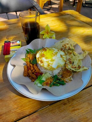 A plate of food with rice, a fried egg, and various vegetables on a wooden table. - Hotel Grand Sumatera (Surabaya)