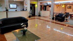 A spacious lobby with a reception desk, a black leather sofa, a glass coffee table with flowers, and a staircase in the background. - Hotel Grand Sumatera (Surabaya)