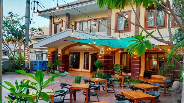 An outdoor seating area with tables and chairs, surrounded by plants and a building with a sign reading "ERASKA". - Hotel Grand Sumatera (Surabaya)
