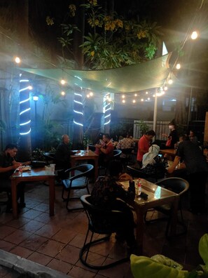 An outdoor dining area with tables and chairs, string lights, and plants. - Hotel Grand Sumatera (Surabaya)