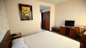 A hotel room with a large bed, a television, a wooden desk, and a framed picture on the wall. - Hotel Grand Sumatera (Surabaya)