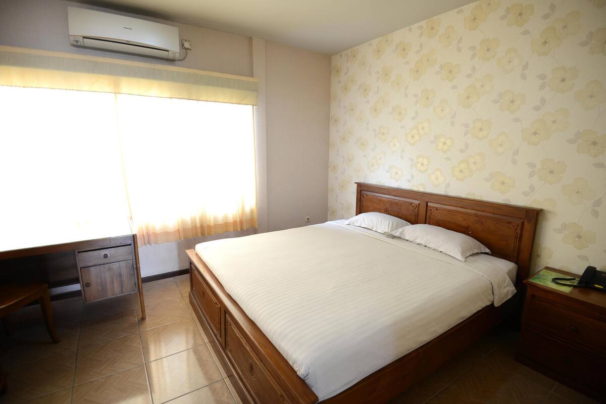 Un dormitorio con cama de madera, mesita de noche, escritorio y ventana con cortinas.