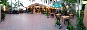 A hotel entrance with a covered patio area, outdoor seating, and a parking area with motorcycles. - Hotel Grand Sumatera (Surabaya)