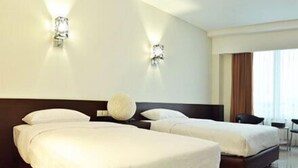 Quarto de hotel com duas camas, um objeto decorativo redondo e grande na cabeceira e vista da cidade pela janela.