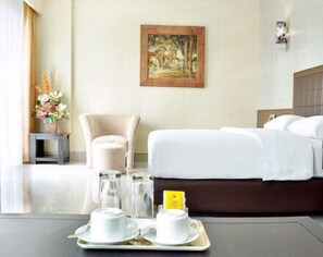A hotel room with a bed, a chair, a painting on the wall, and a tray with cups and a phone. - Bamboo Inn Hotel & Cafe (Jakarta)