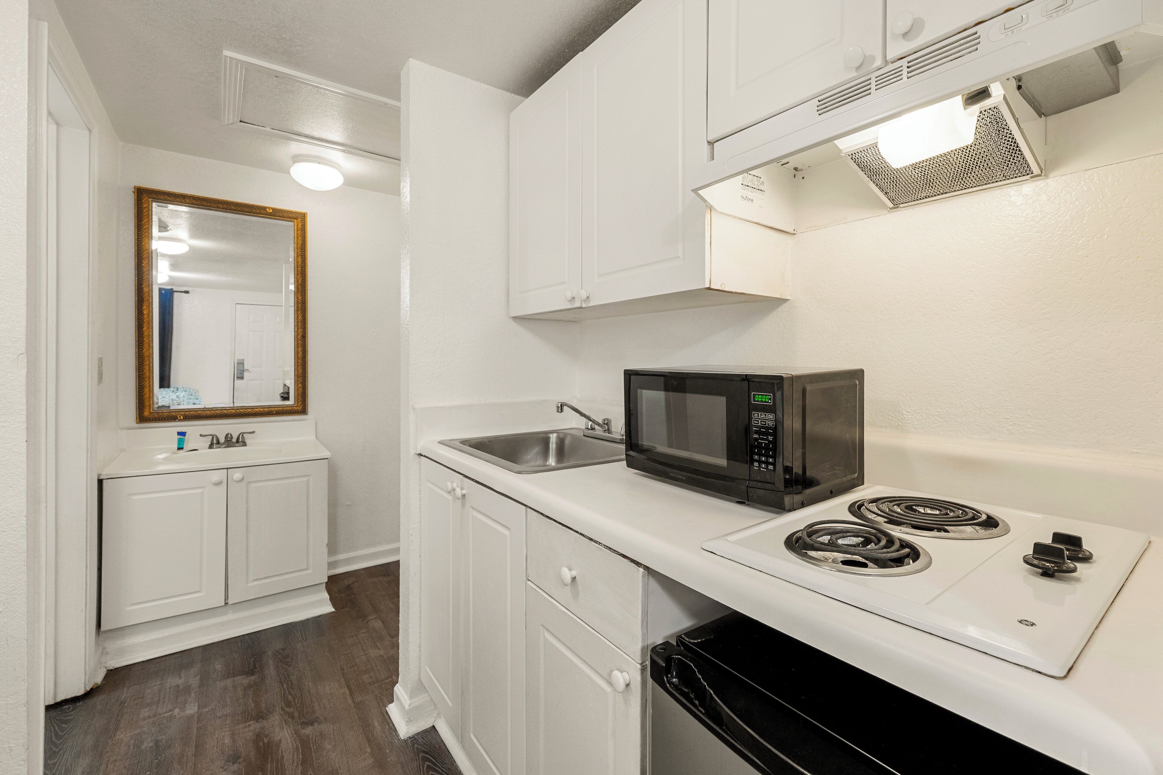 A compact kitchen with white cabinetry, a stainless steel sink, a black microwave, and a stove with four burners.