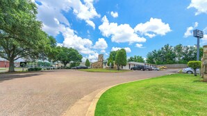 A suburban street with a grassy median, a stone building, and parked cars.