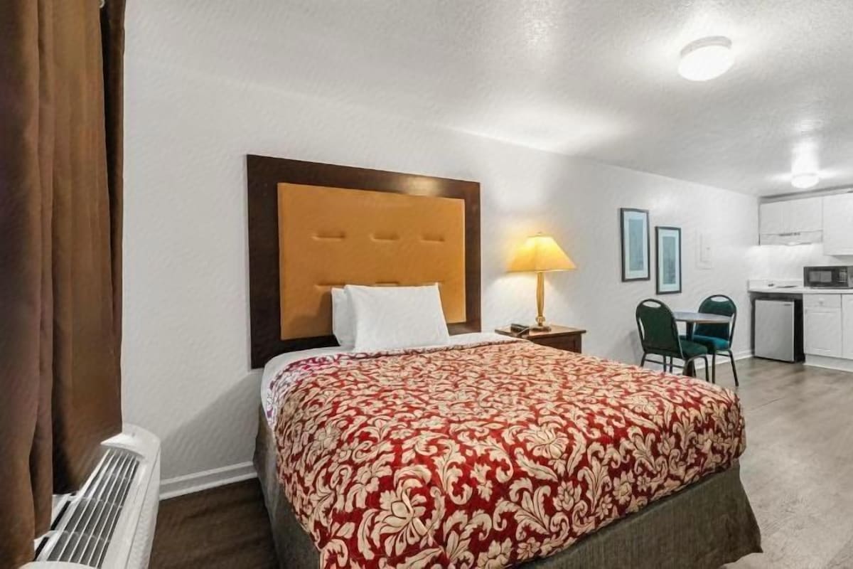 A hotel room with a bed, a desk, a chair, and a kitchenette.