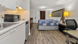 A hotel room with a bed, desk, chair, microwave, and kitchenette.