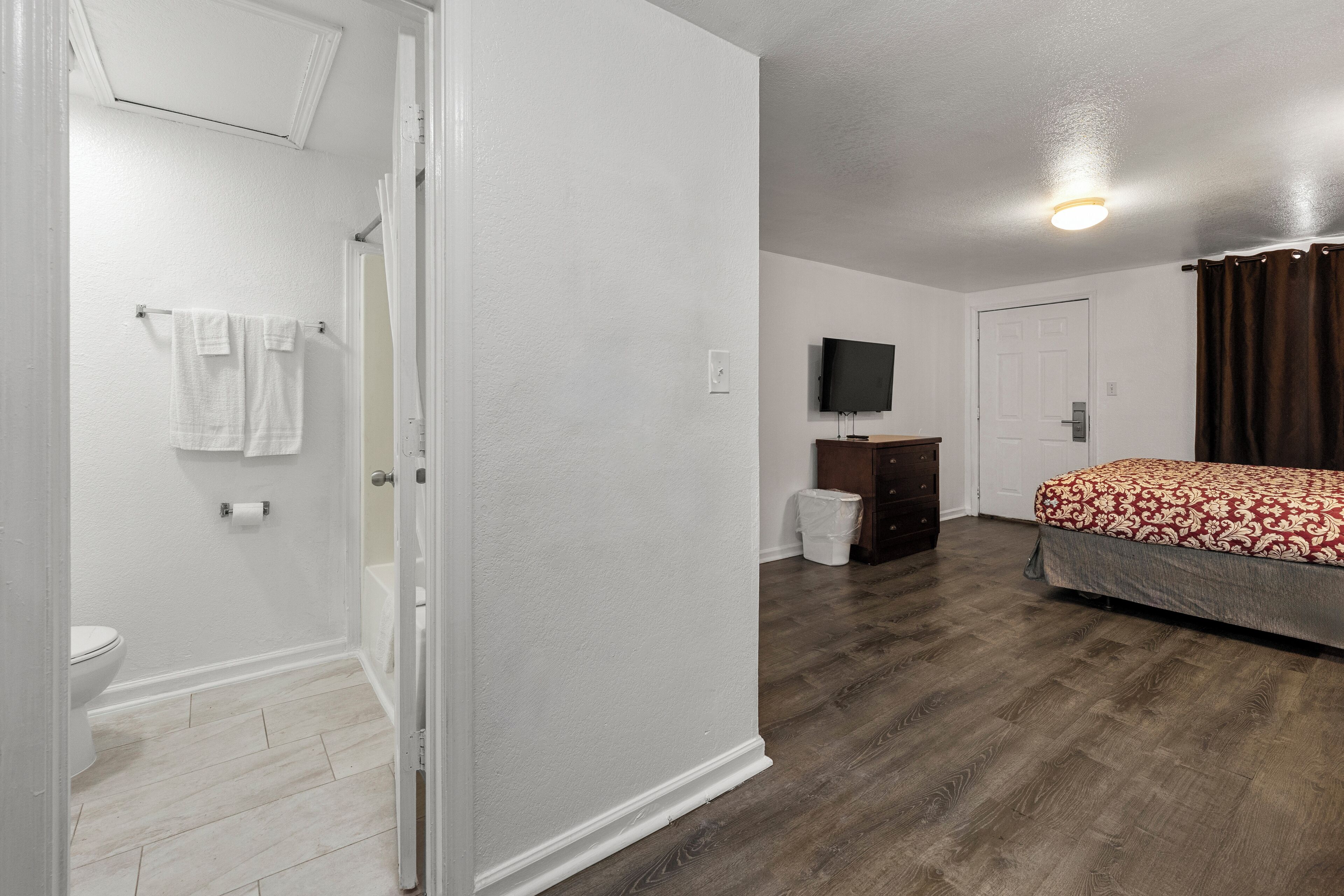 A bedroom with a bed, a television, a dresser, and a bathroom with a toilet and towel rack.