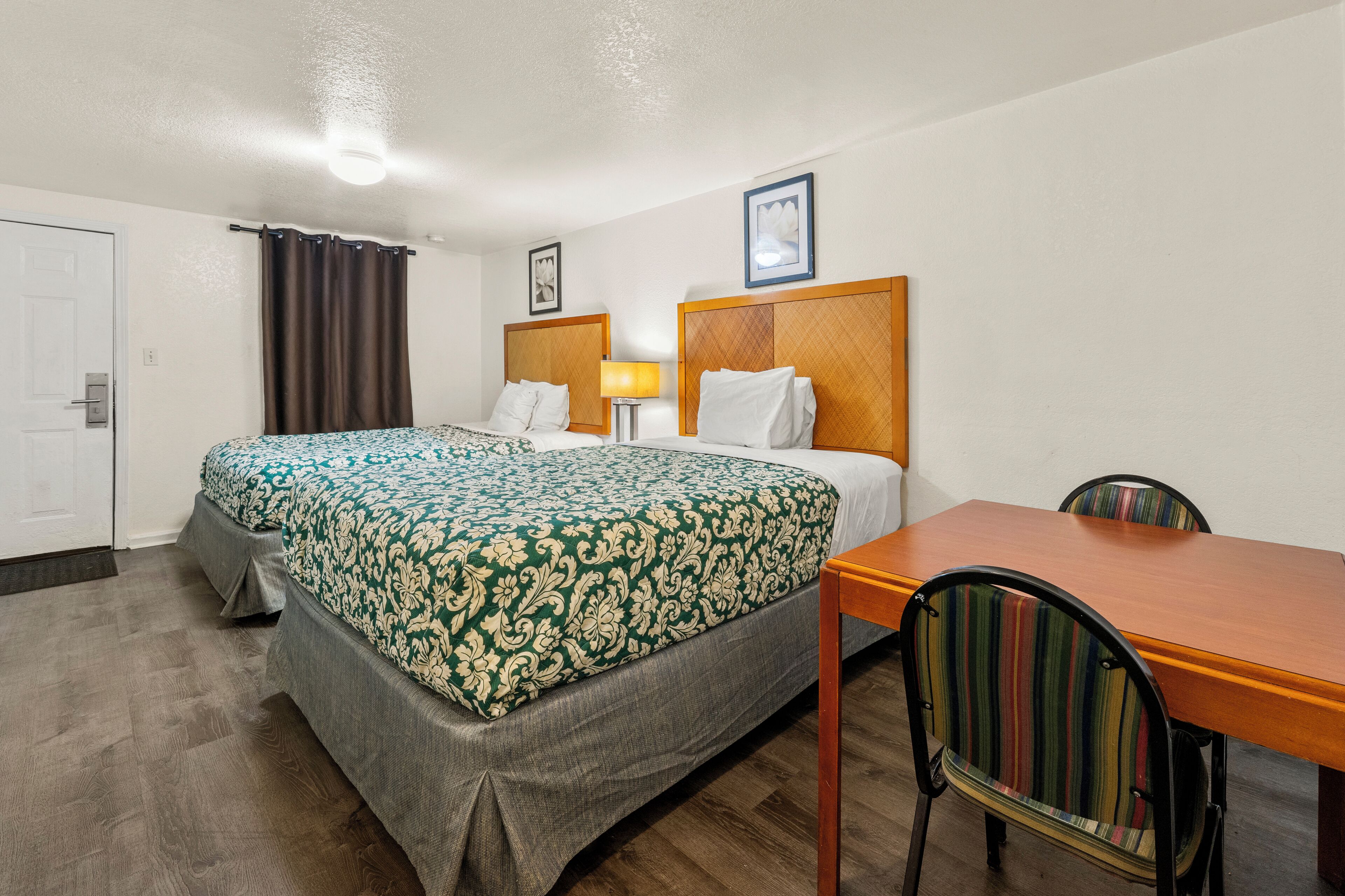 Une chambre d’hôtel avec un lit double, une table en bois, une chaise, une lampe et une porte.