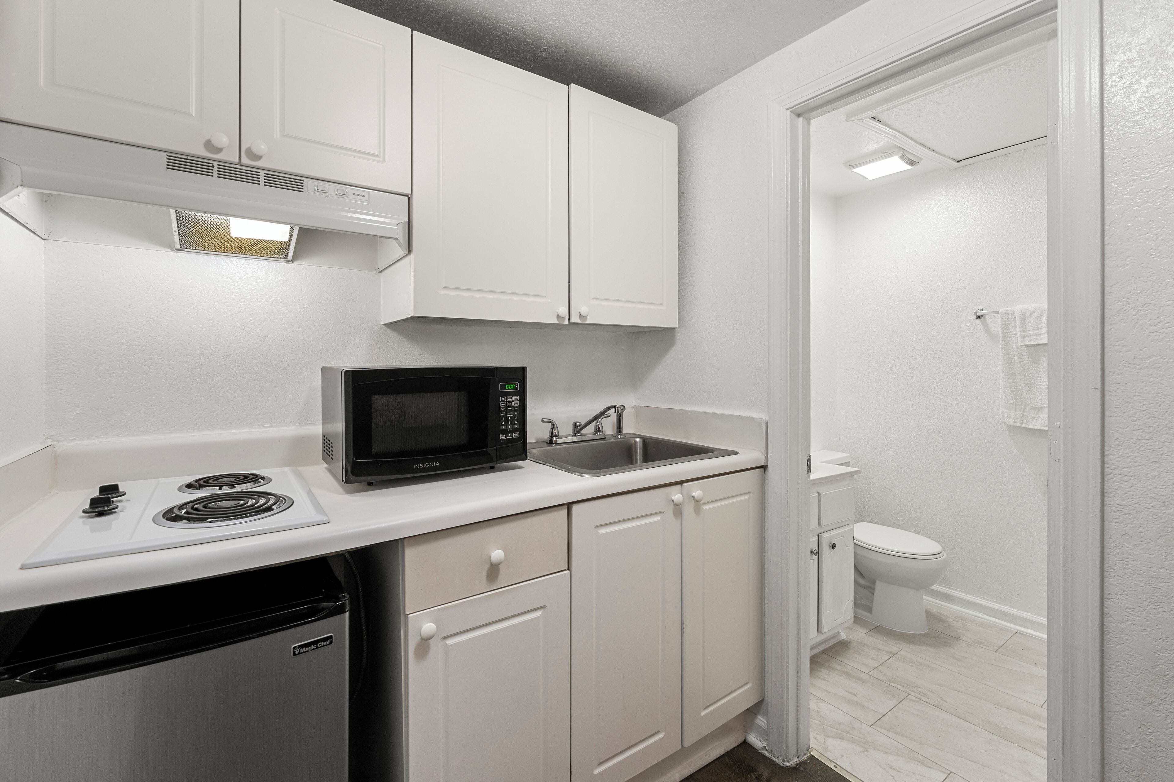 A compact kitchen with white cabinetry, a microwave, a sink, and a dishwasher.