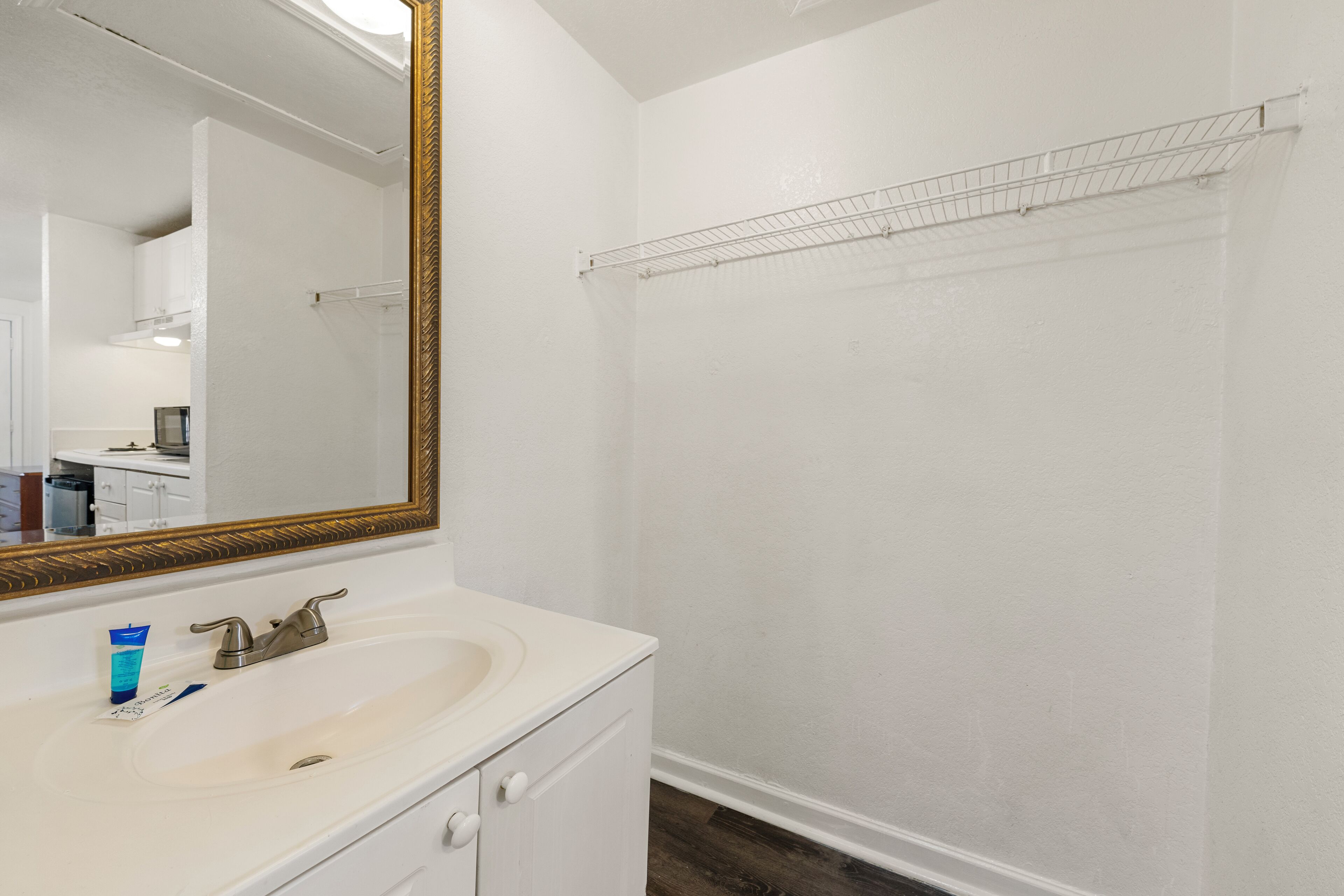 A bathroom with a white sink, a large mirror with a gold frame, and a shower area with a metal shelf.