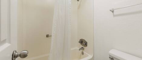 A bathroom with a bathtub, a shower curtain, and a toilet.