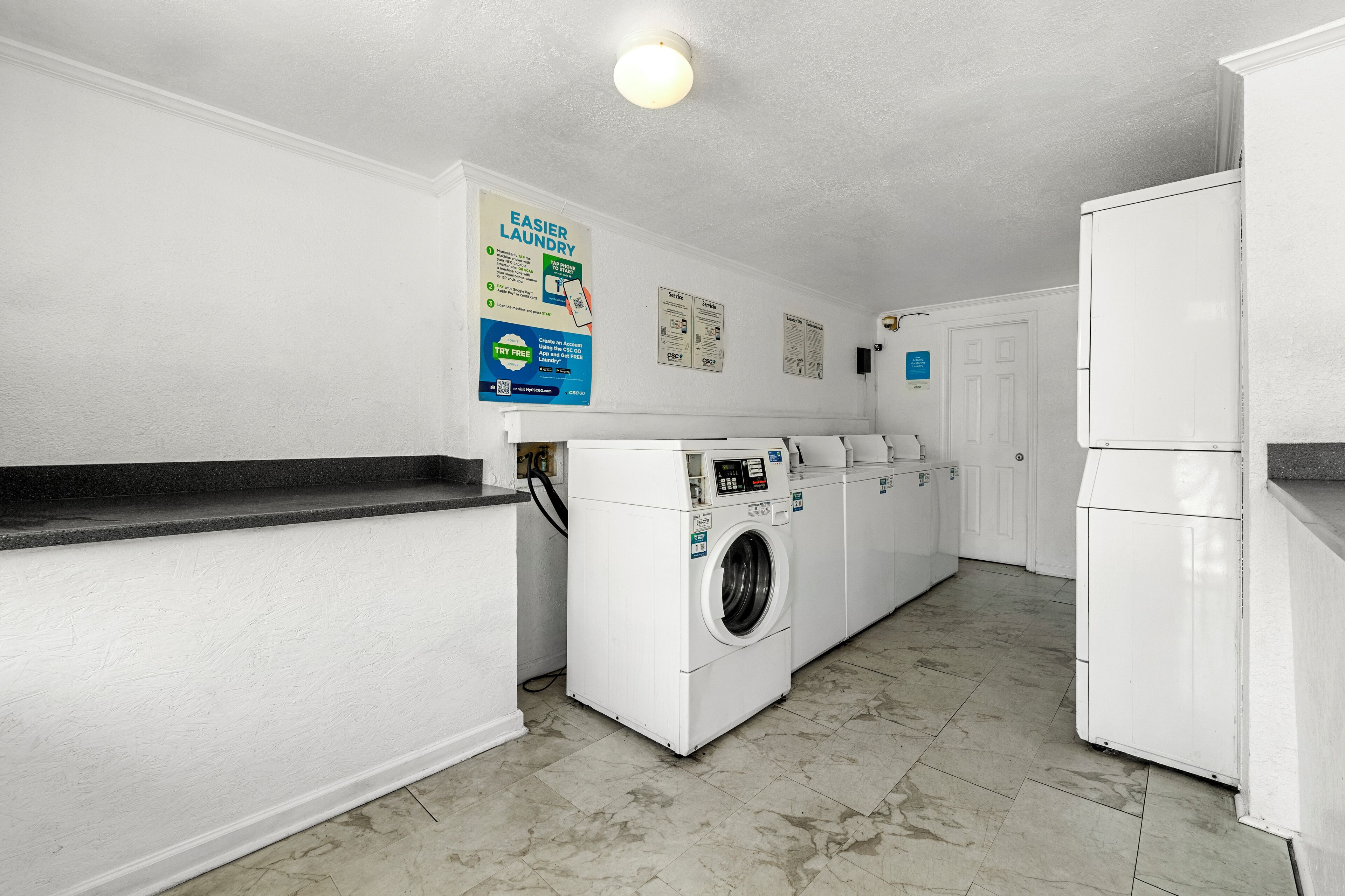 Een wasserette met een wasmachine, droger en een koelkast. Er zijn borden aan de muur en een aanrecht met een wasbak.