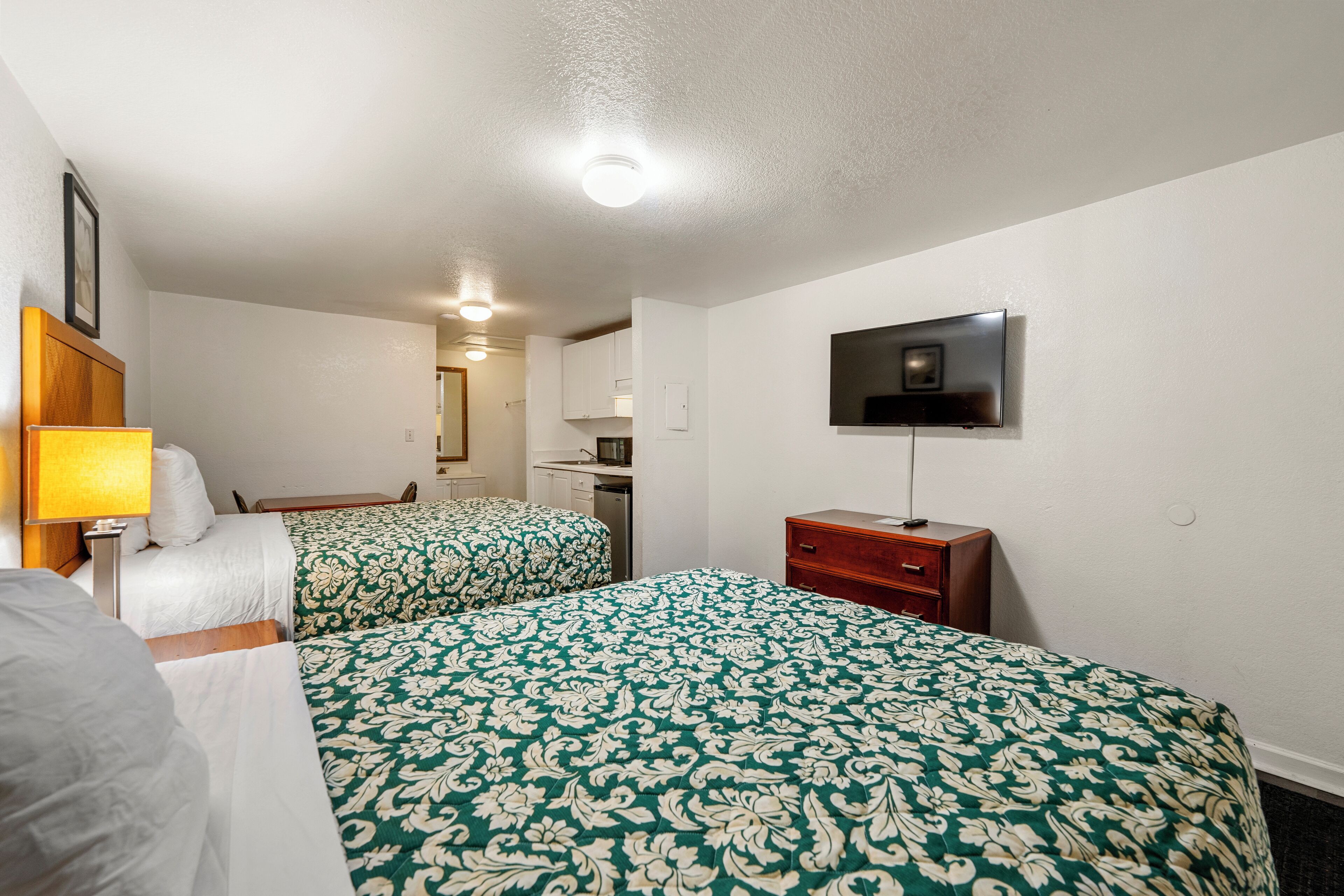 A hotel room with two beds, a TV, a desk, and a lamp.