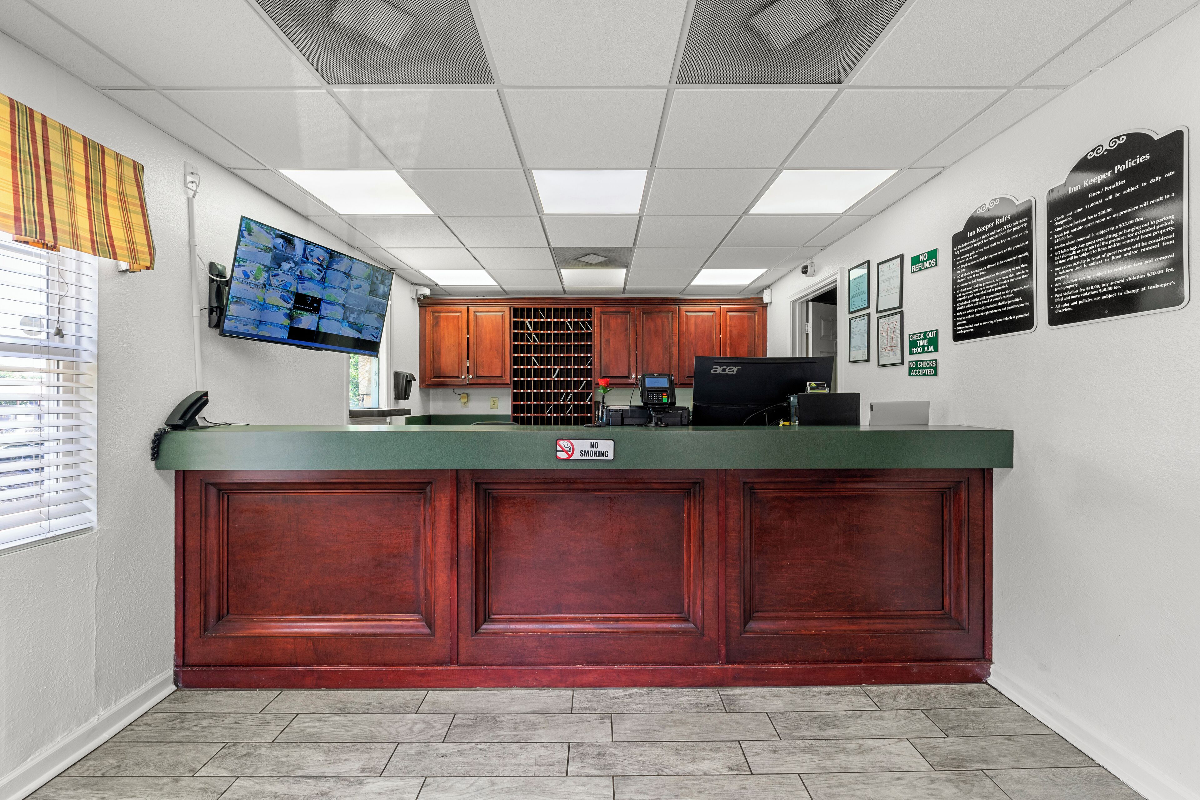 A reception area with a green counter, wooden cabinets, a mounted television, and a no-smoking sign.