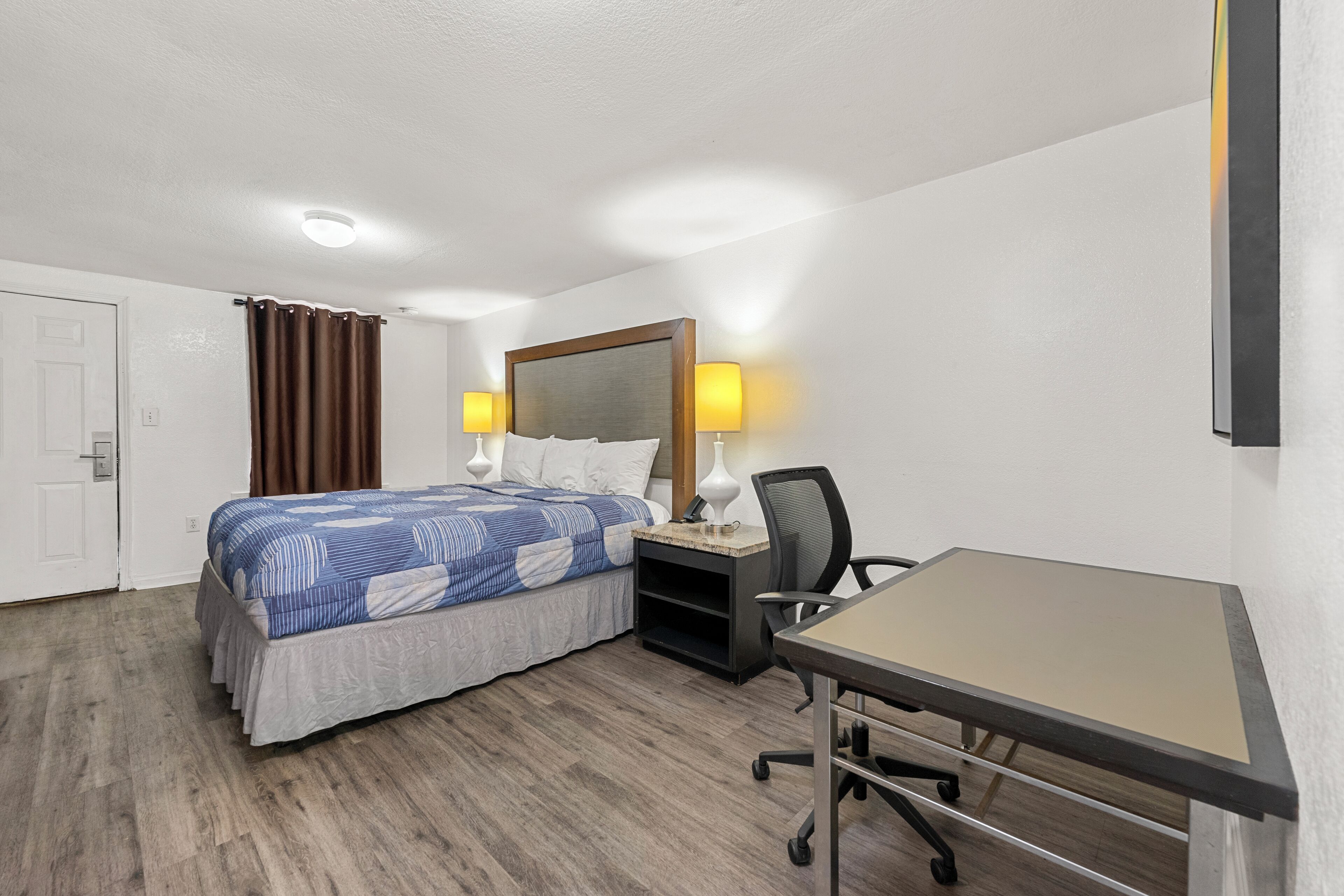 A hotel room with a bed, desk, chair, and two bedside lamps.