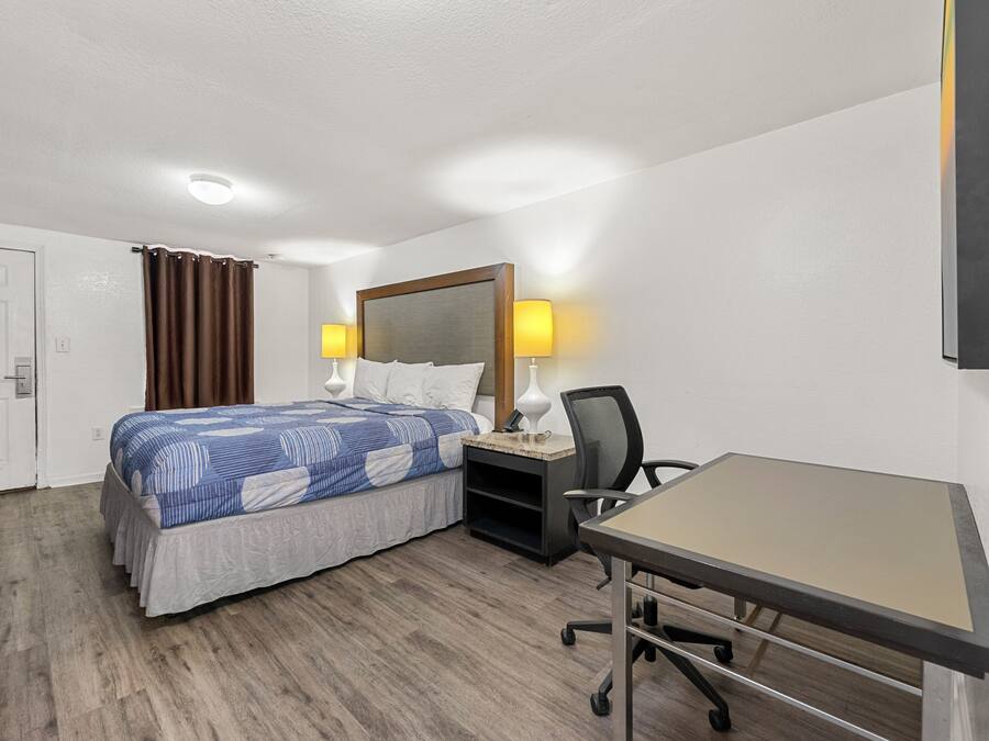 A hotel room with a bed, desk, chair, and two bedside lamps.