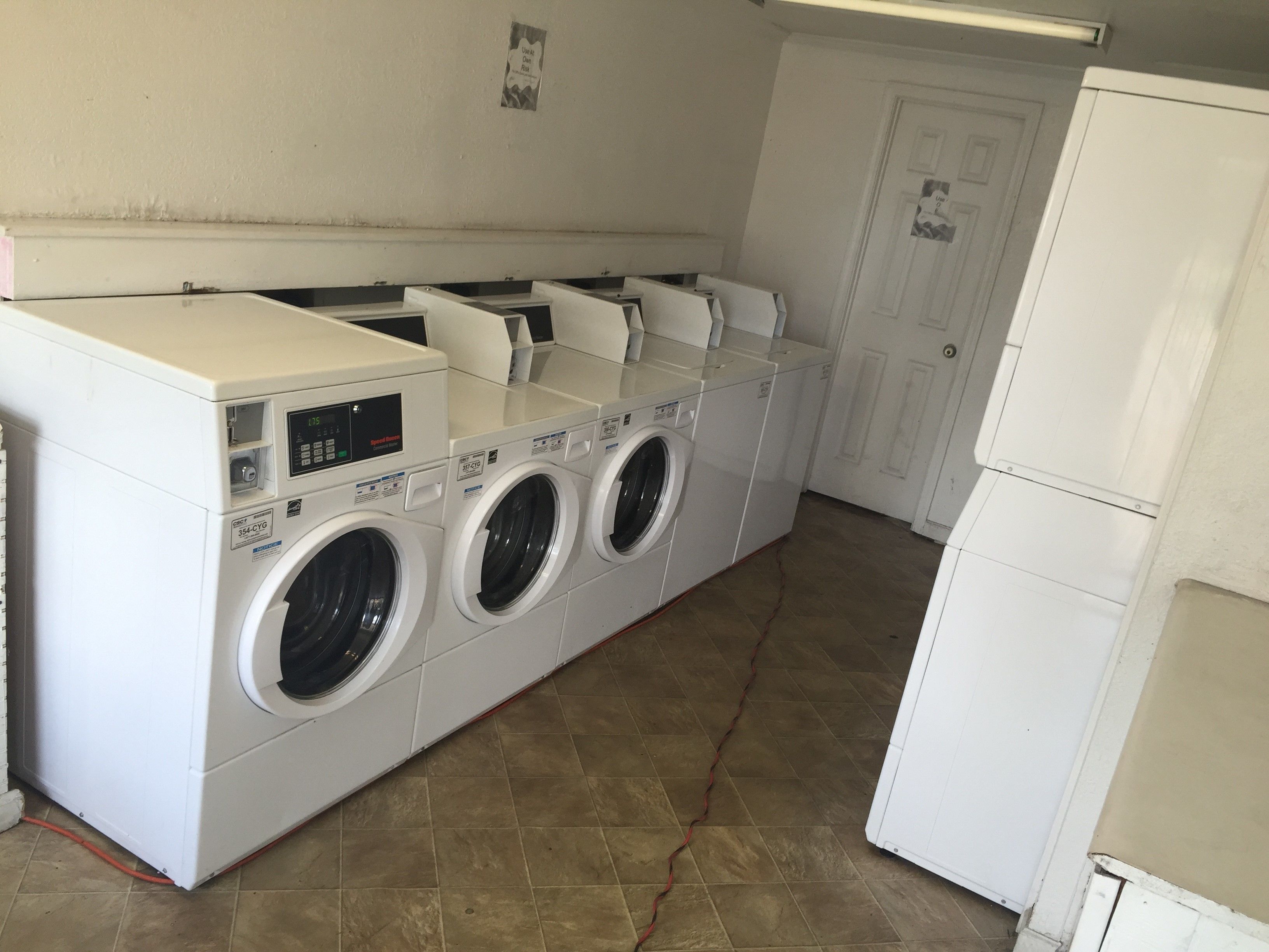 A laundry room with a front-loading washer and dryer, a tiled floor, and a door in the background.