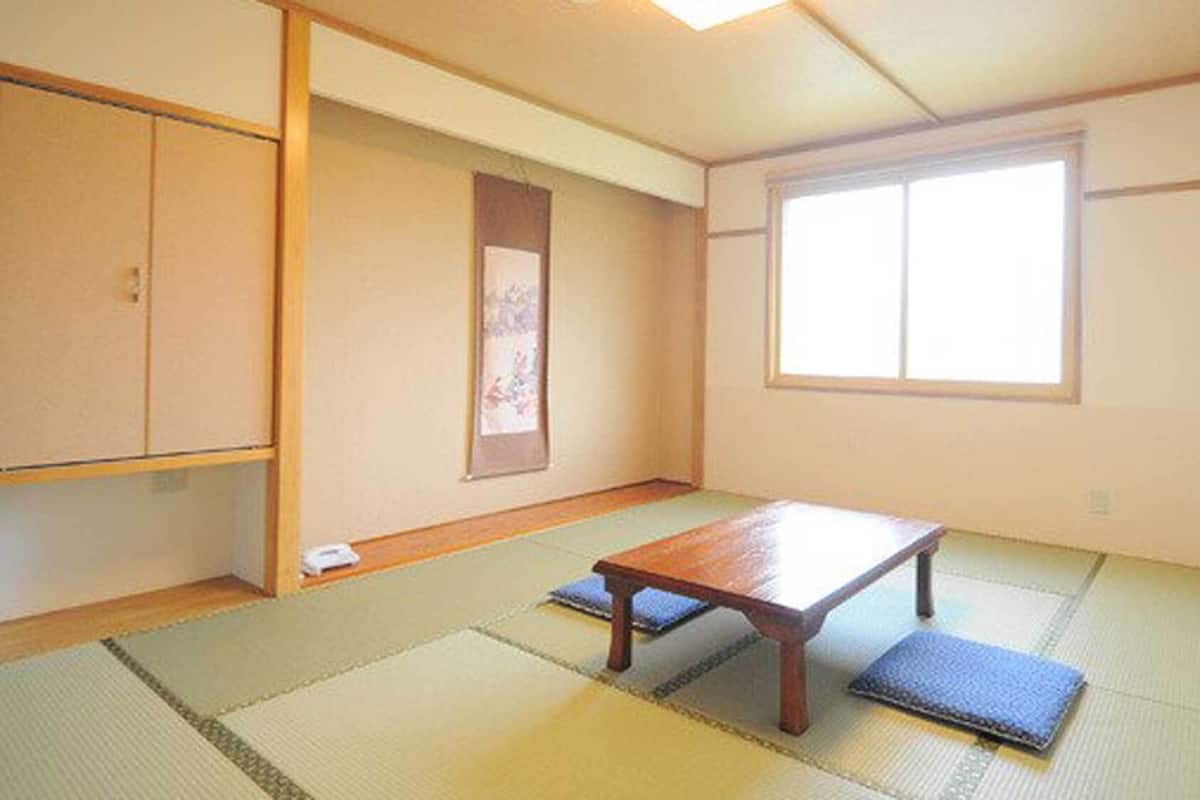Una habitación japonesa tradicional con suelo de tatami, una mesa de madera baja, una puerta corredera y un ventanal grande.