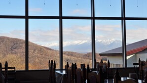 A room with large windows offering a view of a mountain range and a forested area. - Highland Furano (Furano)