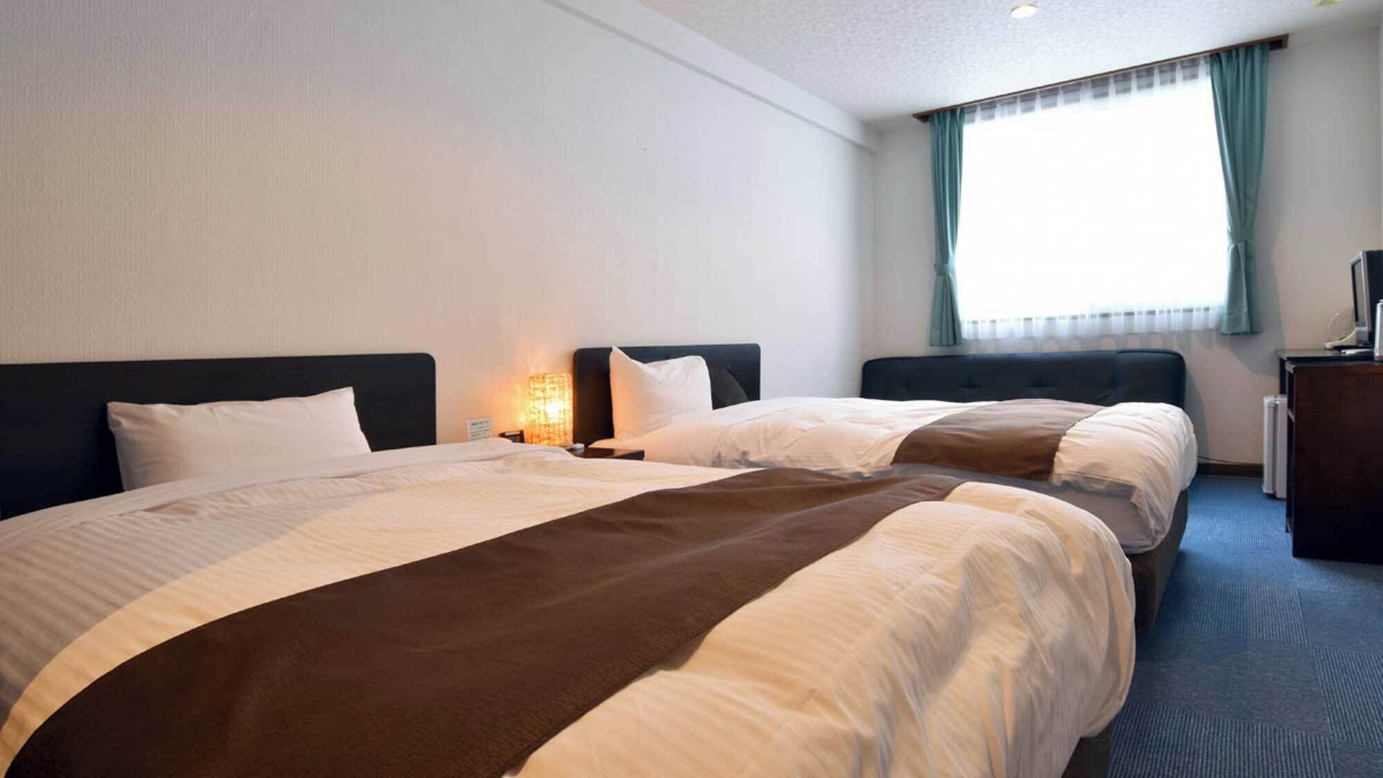 A hotel room with two beds, a desk, a lamp, and a window with curtains.
