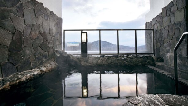 A stone-walled hot spring area with a view of mountains through a window. - Highland Furano (Furano)