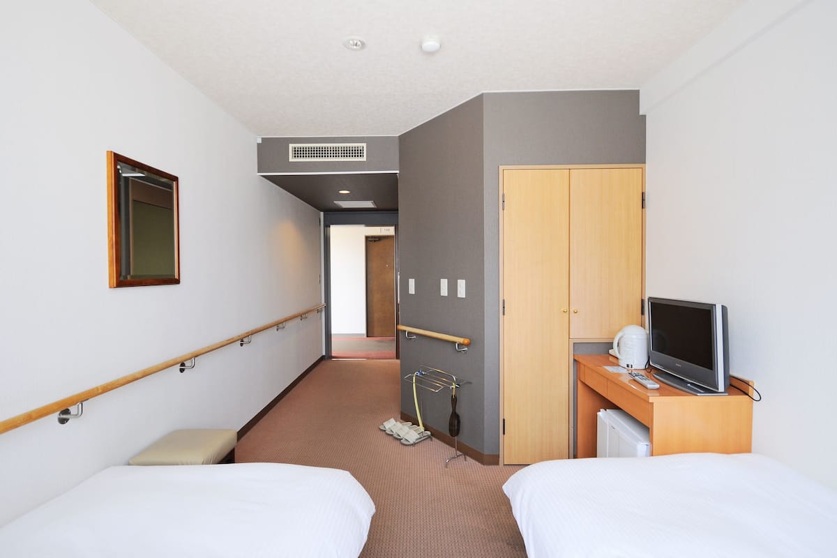 Habitación de hotel con dos camas, televisor, escritorio con computadora, espejo y puerta.