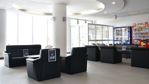 A lobby with a black sofa, a reception desk, vending machines, and a large window. - Highland Furano (Furano)