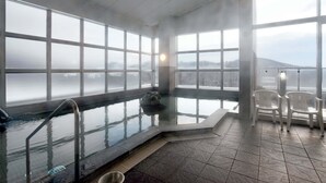 A large indoor swimming pool with clear views of a mountainous landscape through large windows. - Highland Furano (Furano)