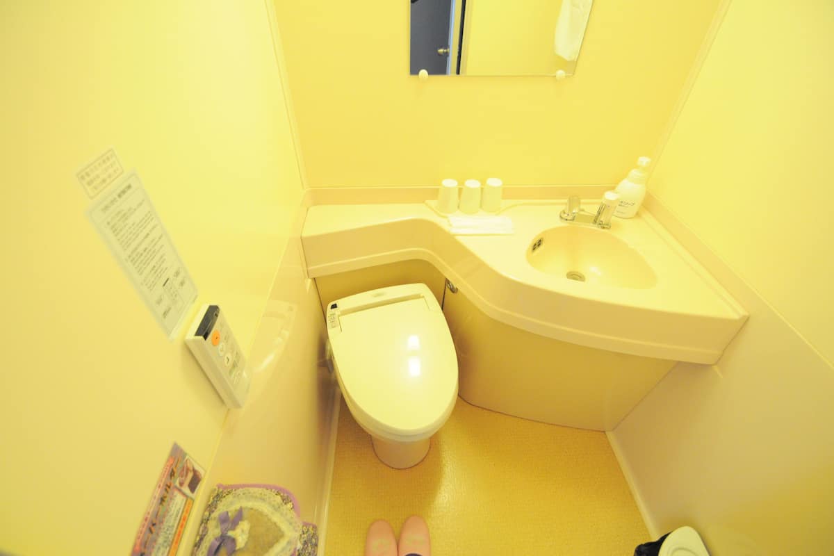 Un baño pequeño con inodoro, lavamanos y espejo. Hay artículos de aseo en la encimera.