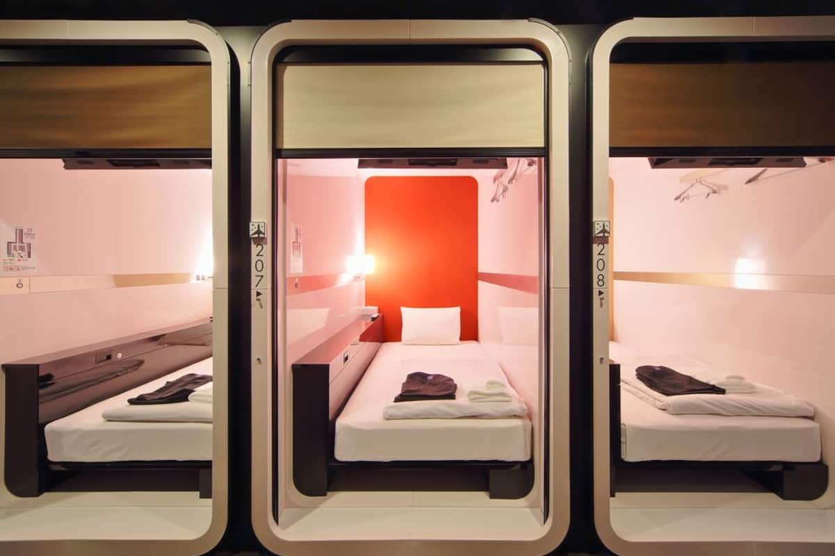 A hotel room with three beds arranged in a row, each with a wooden headboard and white bedding.