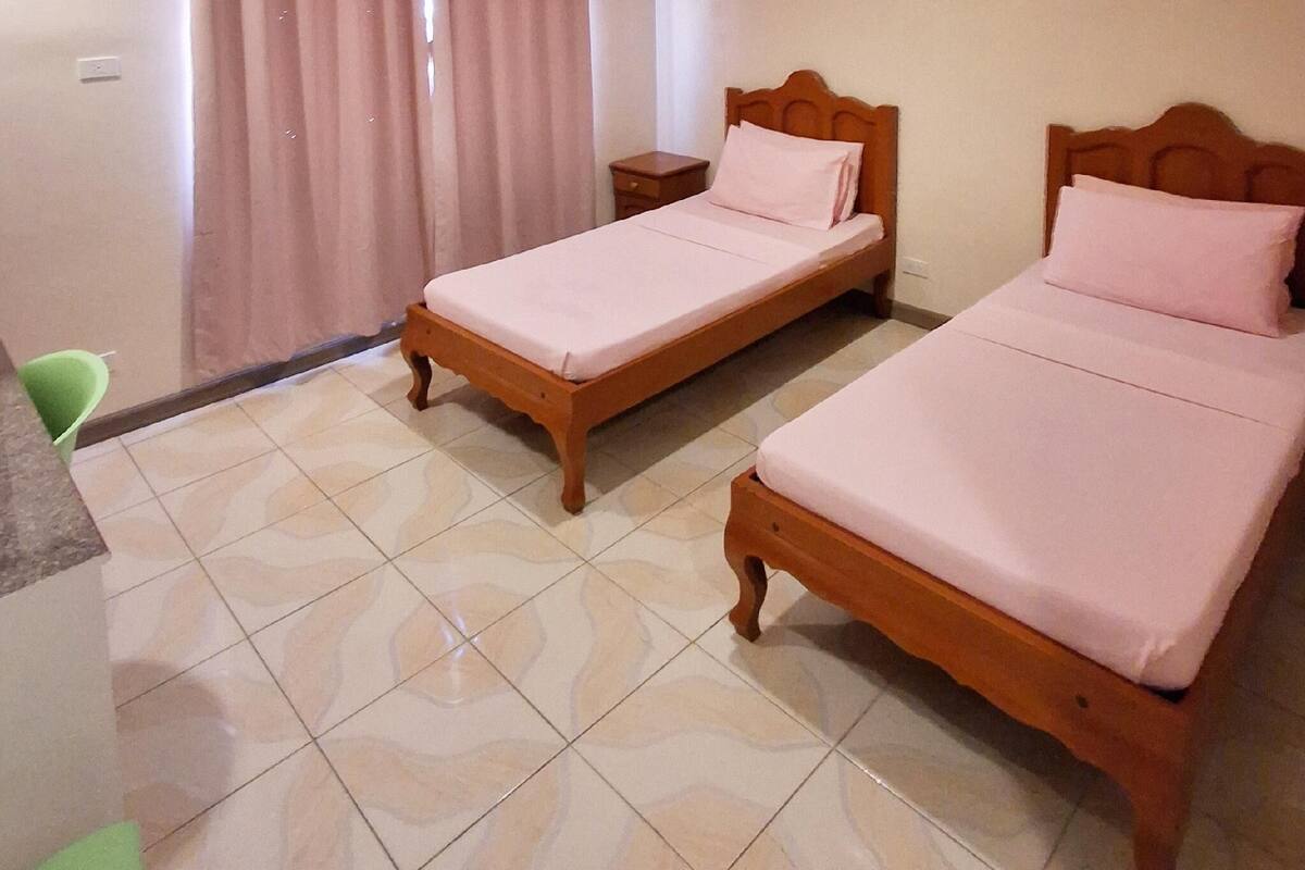 A room with two wooden beds, a small bedside table, a chair, and a curtain.