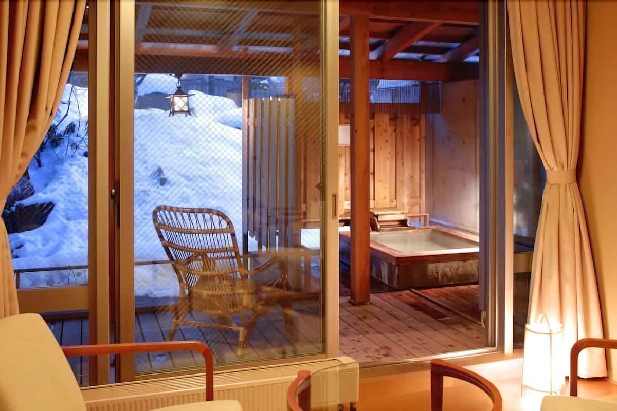 Una cabana de fusta amb una porta de vidre que dona a una terrassa amb una cadira i un banyera hidromassatge.