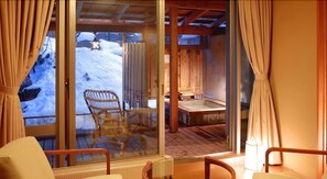 A wooden cabin with a glass door leading to a deck with a chair and a hot tub.