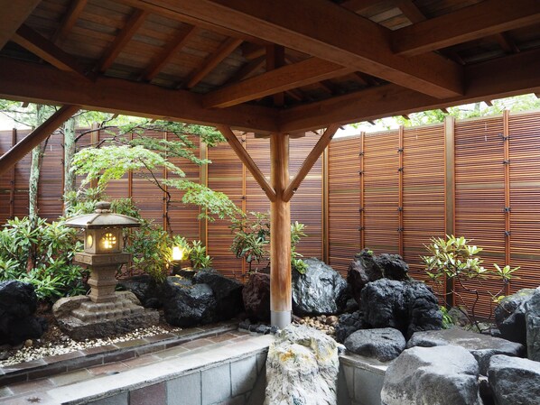 A traditional Japanese garden with a stone lantern, bamboo fence, and rock formations.