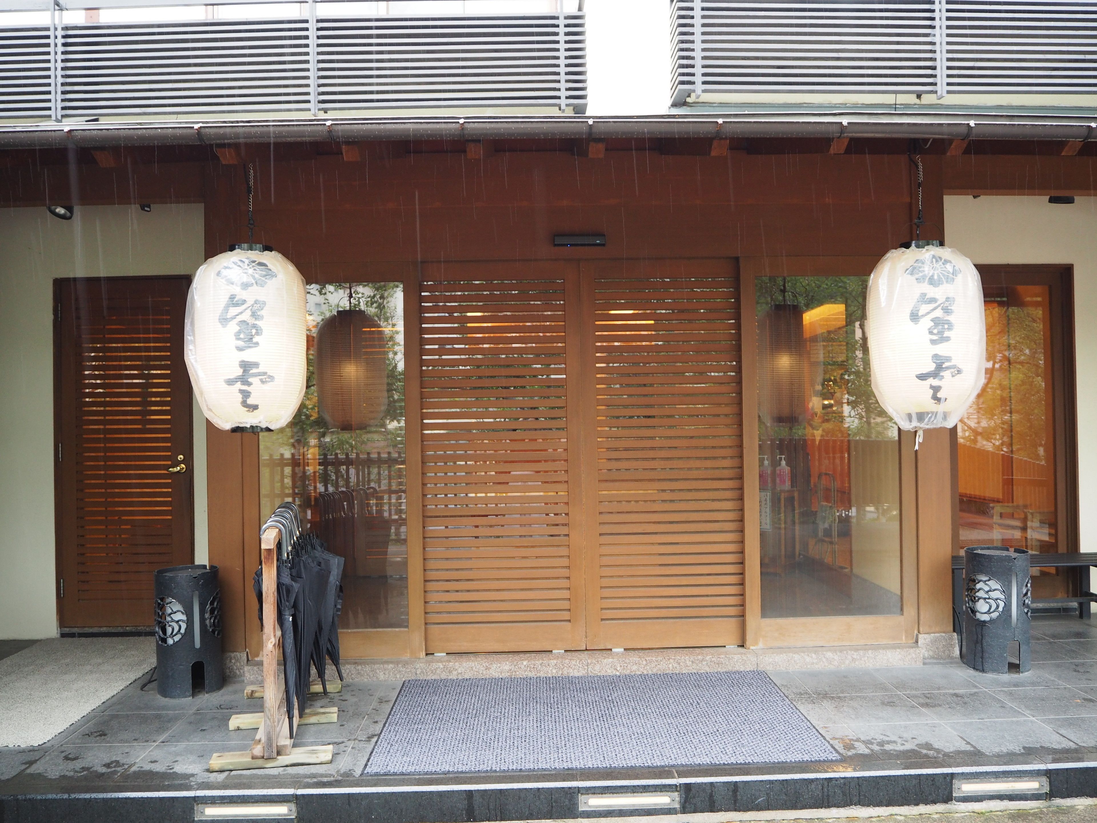 A traditional Japanese building with sliding doors, a wooden entrance, and two hanging lanterns.