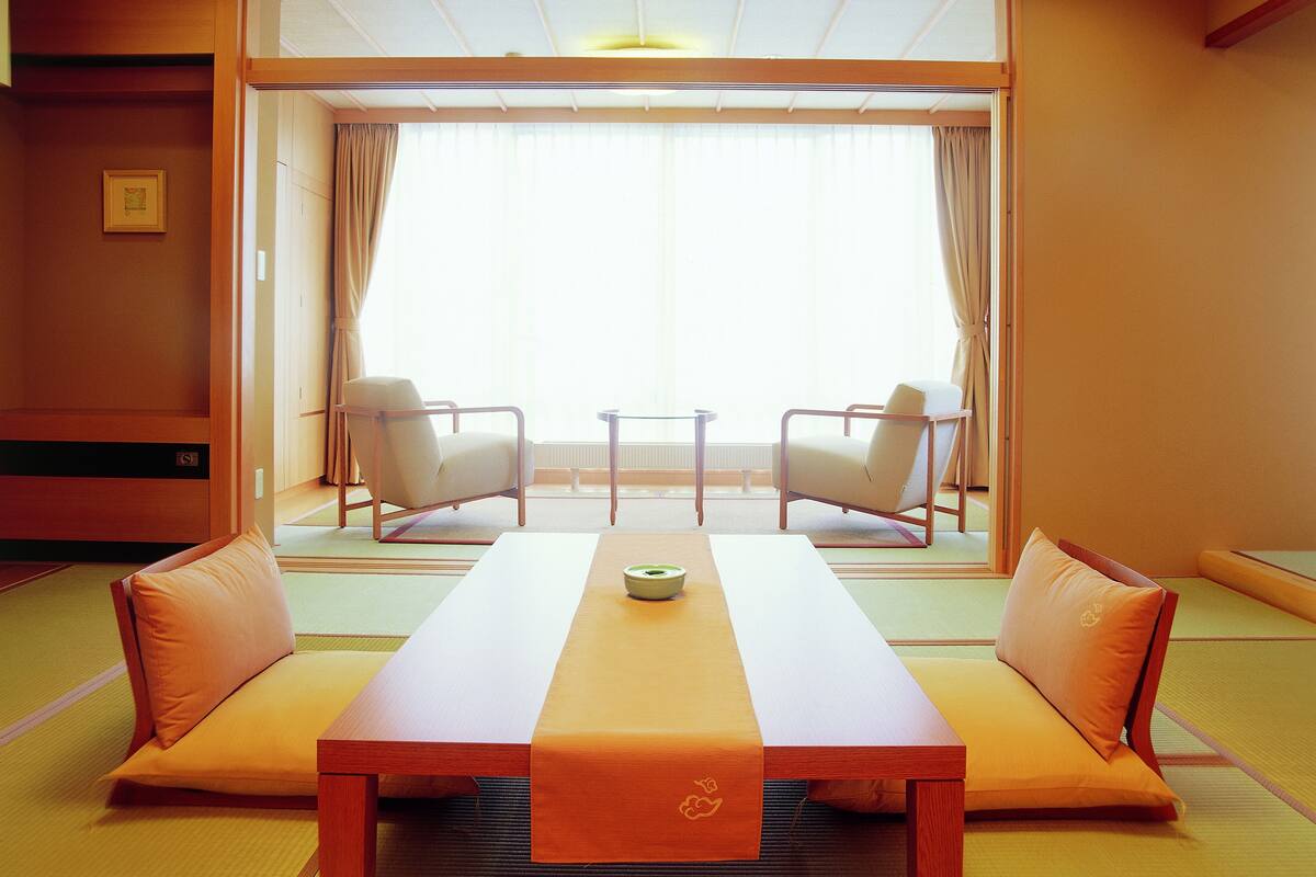 Una habitació japonesa tradicional amb fons de tatami, una taula baixa amb coixins i dues cadires.