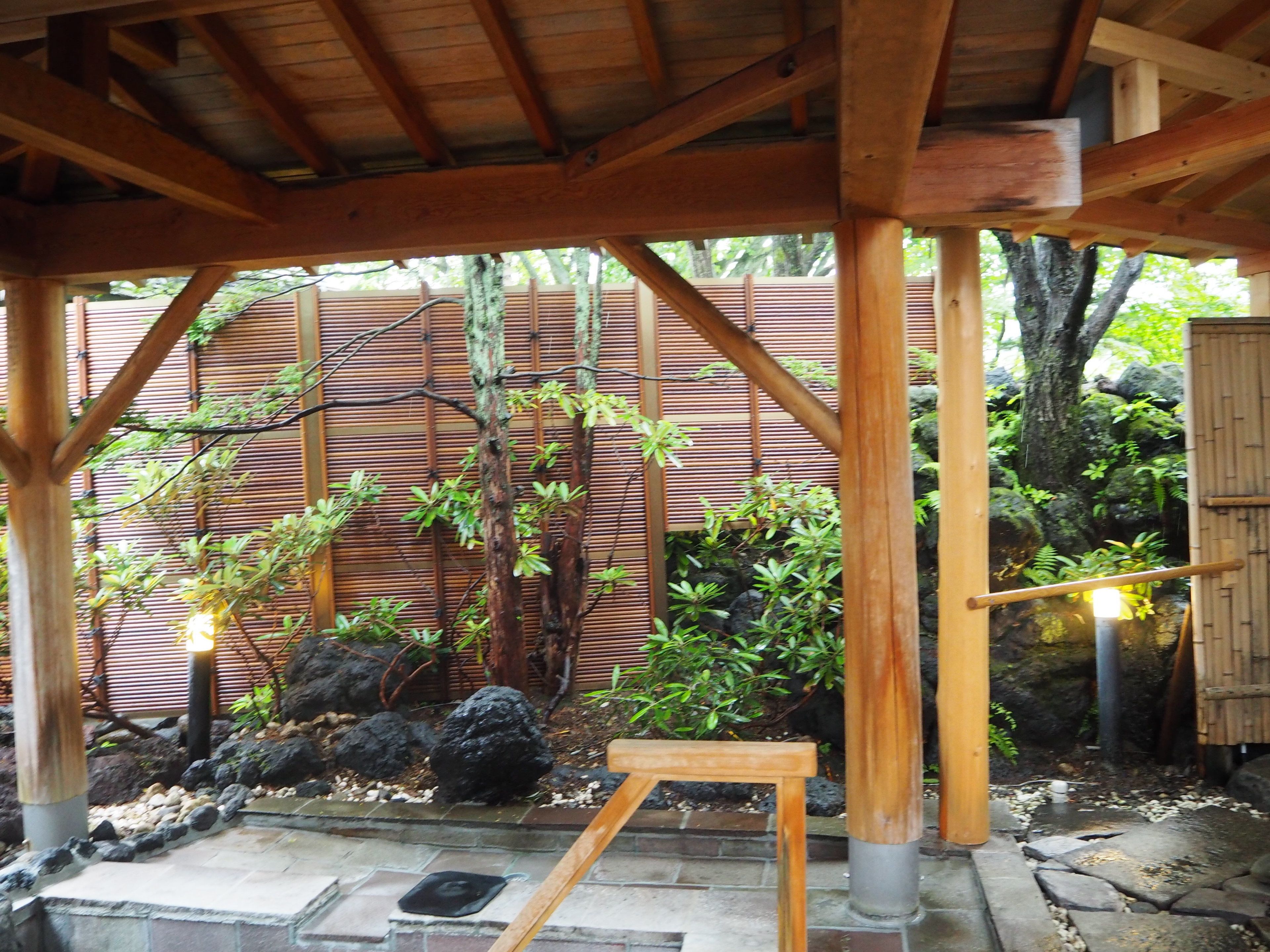 A covered outdoor area with wooden beams, bamboo fencing, and various plants.