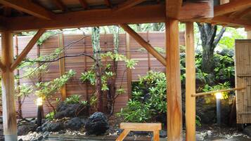 A covered outdoor area with wooden beams, bamboo fencing, and various plants.