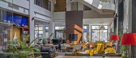 A spacious lobby with a high ceiling, a central staircase, and a seating area with yellow chairs.