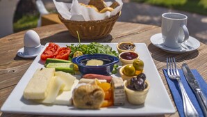 Uma mesa de café da manhã com diversos alimentos, uma xícara e vista para o mar e palmeiras.