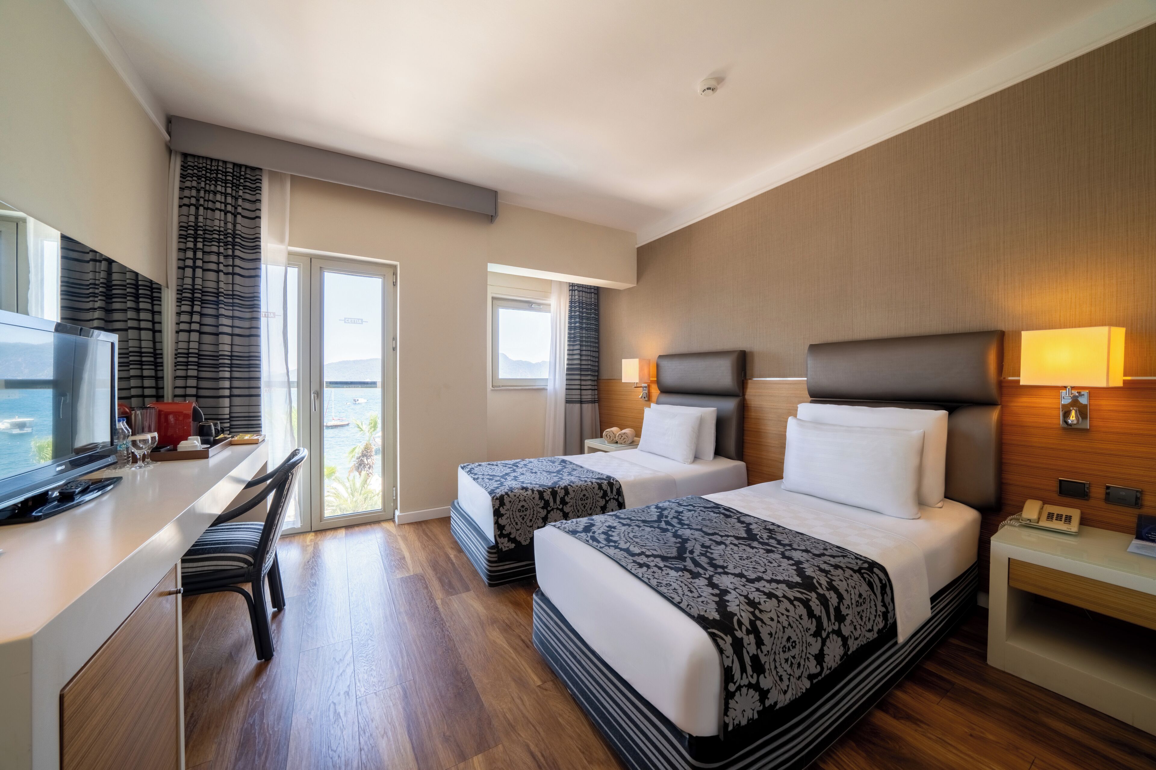 Habitación de hotel con dos camas, un escritorio, un televisor y un balcón con vistas.